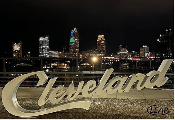 Photo by Beth Glas, ED of LEAP with the Cleveland script sign and downtown in the background at night. Terminal Tower is lit in blue & green for LEAP in 2024.