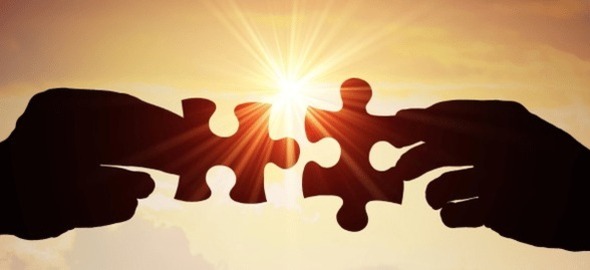 Two hands holding puzzle pieces silhouetted against sun