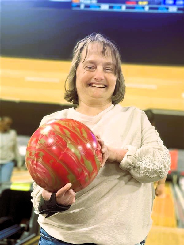 A woman smiles, holding her bowling ball. 